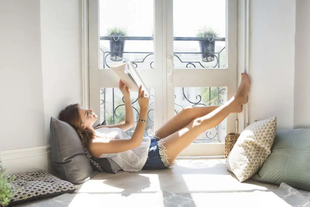 Young pretty girl reading fashion magazine near window